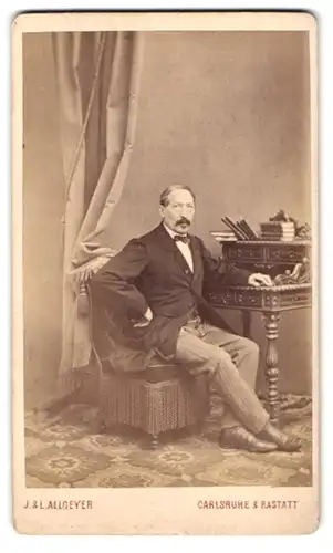 Fotografie J. L. Allgeyer, Carlsruhe, Portrait Herr im Anzug mit Heller Hose sitzend am Sekretär