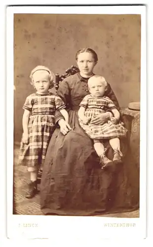 Fotografie J. Linck, Winterthur, Portrait junge Mutter mit zwei Kleinkindern in karierten Kleidern