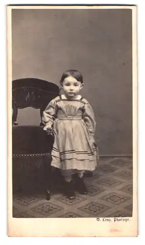 Fotografie D. Lenz, Zürich, Frankengasse 124, Portrait Kleinkind im Pünktchenkleid lehnt an einem Stuhl