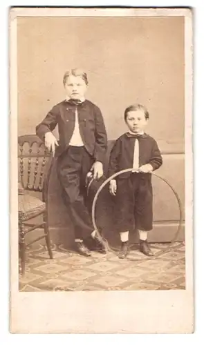 Fotografie Fotograf und Ort unbekannt, Portrait zwei Jungen in Anzügen mit einem Reifen