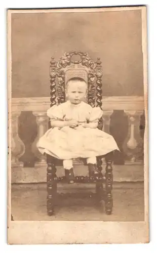 Fotografie Fotograf und Ort unbekannt, Portrait kleines Kind im weissen Kleid sitzend auf einem Stuhl