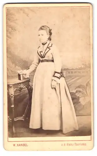 Fotografie W. Kandel, Saarlouis, v. d. französ. Thor, Portrait junge Frau im Biedermeierkleid vor einer Studiokulisse