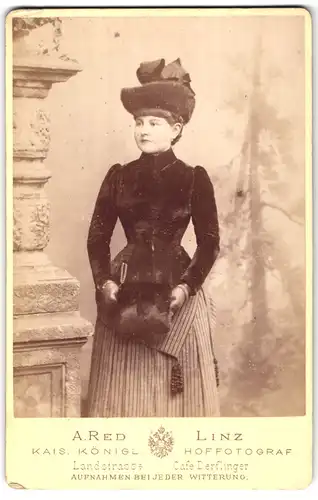 Fotografie A. Red, Linz, Landstr., Portrait junge Frau im Kleid mit Pelzhut und Muff
