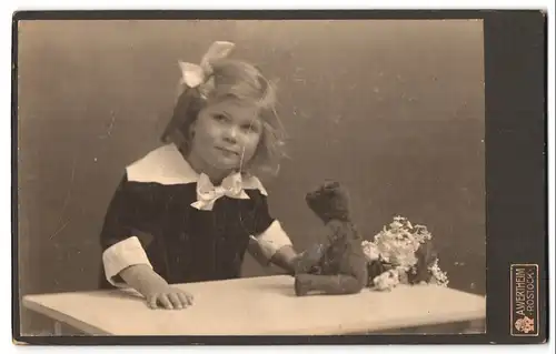 Fotografie A. Wertheim, Rostock, Portrait kleines Mädchen im Kleid mit Teddybär auf dem Tisch