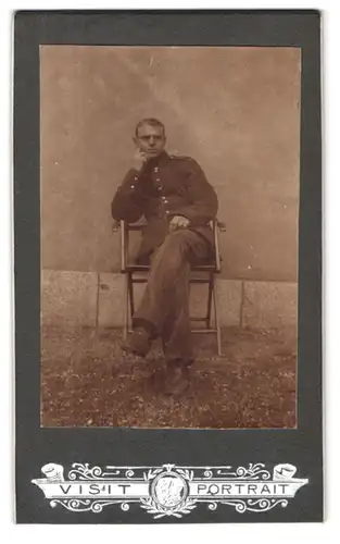 Fotografie unbekannter Fotograf und Ort, Portrait Soldat vor dem Haus sitzend