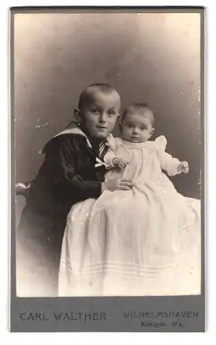 Fotografie Carl Walther, Wilhelmshaven, Königstrasse 57 a, Portrait kleiner Junge im Matrosenanzug mit einem Baby