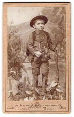 Fotografie Josef Benzinger, Schrobenhausen, Portrait junger Knabe im Jägersgewand mit Flinte und Schwarzpulverbeutel