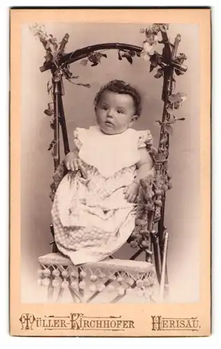 Fotografie Müller Kirchhofer, Herisau, Casernenstr. 68, Portrait Kleinkind mit Locken sitzt in einem Weidenkorb