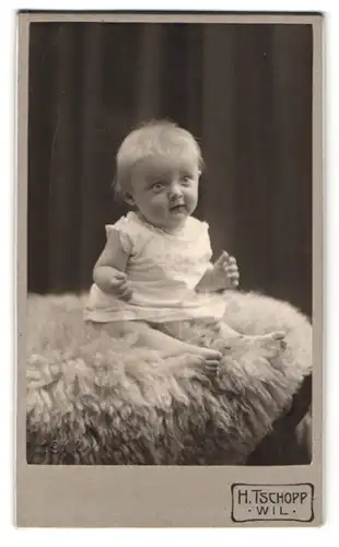 Fotografie H. Tschopp, Wil, Mattstrasse, niedliches Kleinkind auf Fell sitzend