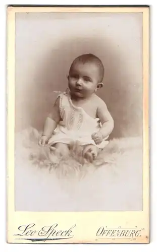 Fotografie Leo Speck, Offenburg, niedliches Baby auf Fell sitzend