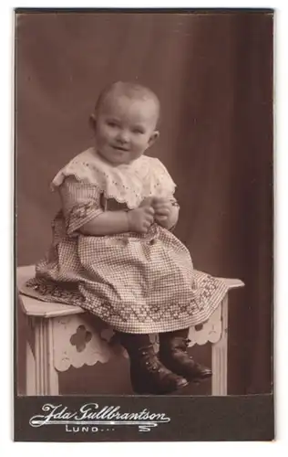 Fotografie Ida Gullbrantson, Lund, Stortorget 4, Portrait Kleinkind im karierten Kleid grinst in die Kamera