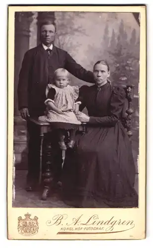 Fotografie B. A. Lindgren, Lund, Grönegatan 15, Portrait Familie mit Kleinkind im Blümchenkleid vor einer Studiokulisse