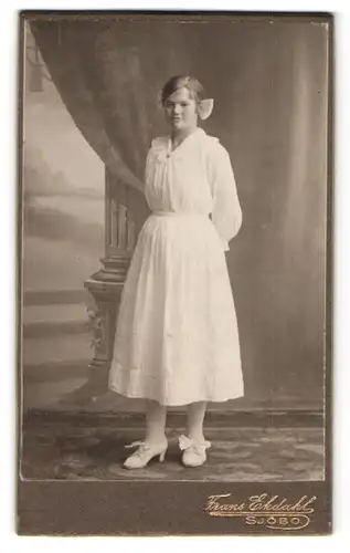 Fotografie Frans Ekdahl, Sjöbo, Portrait junge Frau im weissen Kleid mit Haarschleife und weissen Schuhen