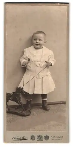 Fotografie Albert Meyer, Hannover, Georgstr. 24, Portrait Kleinkind im weissen Kleid mit Spielzeug Pferd