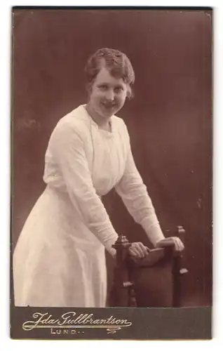 Fotografie Ida Gullbrantson, Lund, Stortorget 4, Frau im weissen Kleid stütz sich auf einen Stuhl