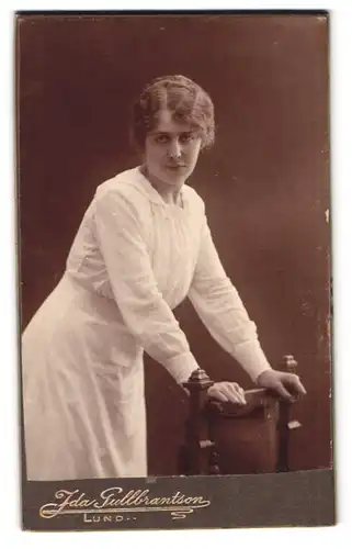 Fotografie Ida Gullbrantson, Lund, Stortorget 4, Portrait Frau im weissen Kleid auf Stuhl abstützend