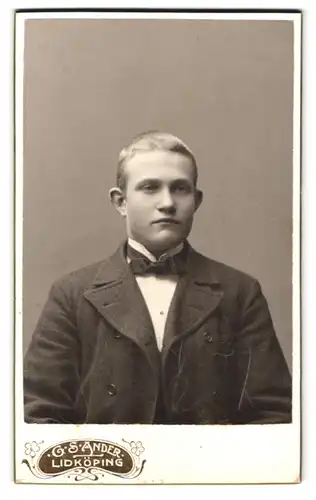 Fotografie G. S. Ander, Lidköping, Portrait junger Mann im Stoffanzug mit Fliege und Segelohren