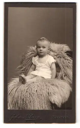 Fotografie John Nilsson, Kalmar, Portrait kleines Kind im Kleidchen sitzt auf einem Fell