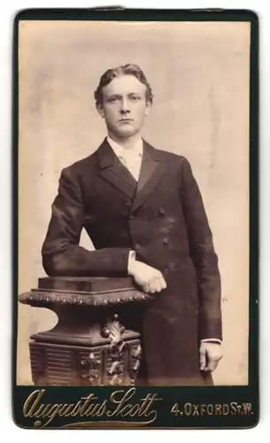 Fotografie Augustus Scott, London, Oxford St. 4, Portrait junger Mann im Anzug lehnt an einem Podest