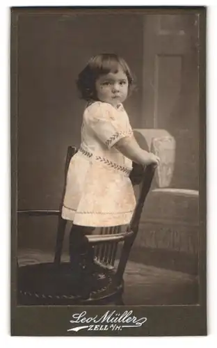 Fotografie Leo Müller, Zell a. H., niedliches Mädchen im Kleid auf Stuhl stehend