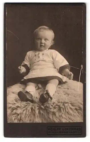 Fotografie Köhler & Saemann, Halberstadt, Heinrich Juliusstr. 8, Portrait Kleinkind im Kleid auf einem Fell sitzend