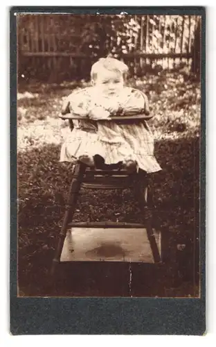 Fotografie Fotograf und Ort unbekannt, Portrait Kleinkind im Kinderstuhl mit Kleid
