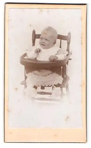 Fotografie Fotograf und Ort unbekannt, Portrait Kleinkind im Kinderstuhl mit Kleid an