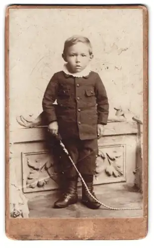 Fotografie Fotograf und Ort unbekannt, Portrait kleiner Junge mit Peitsche im Anzug