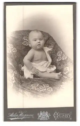 Fotografie Atelier Hagman, Ousby, Niedlicher Säugling sitzend auf dem Sofa