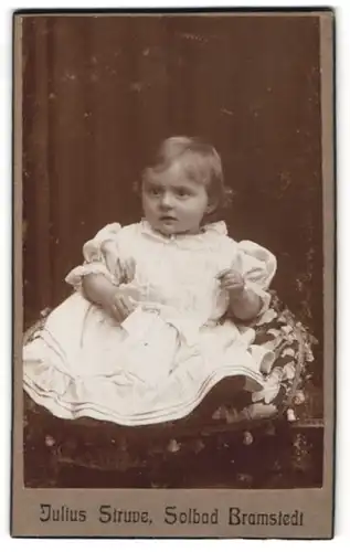 Fotografie Julius Struve, Bad Bramstedt, Portrait kleines Mädchen im weissen Kleid sitzt auf einem Kissen
