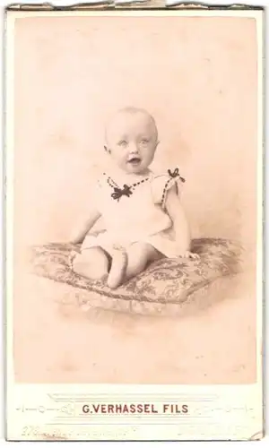 Fotografie G. Verhassel Fils, Bruxelles-Laeken, Portrait süsses Kleinkind im weissen Hemd mit nackigen Füssen