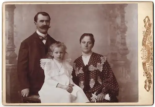 Fotografie Fotograf und Ort unbekannt, Familie mit Tocher in weissen Kleid, Vater mit Walrossbart vor einer Studiokulisse