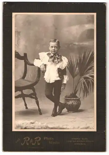 Fotografie R. & R., Chicago, Clark and Madiosn St., Portrait kleiner Junge im Spitzenkleid mit Schleife