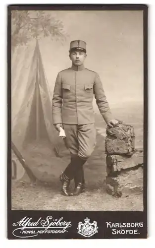 Fotografie Alfred Sjöberg, Karlsborg, Portrait schwedischer Soldat in Uniform Rgt. 4 vor einer Studiokulisse