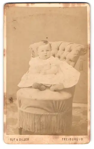 Fotografie Ruf & Dilger, Freiburg i. B., Ludwigstr. 2, Baby im Taufkleid auf Sessel sitzend