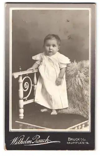 Fotografie Wilhelm Rauch, Bruck, Hauptplatz 12, niedliches kleines Kind in Leinenkleid auf Stuhl stehend