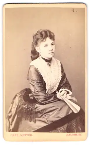 Fotografie Gebr. Matter, Mannheim, P 7. 19 u. 8, Portrait junge Frai im seidenen Kleid mit Fächer und Locken