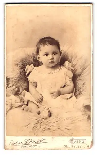 Fotografie Oskar Schmidt, Mainz, Stadthausstr. 4, Portrait kleines Kind im weissen Kleidchen sitzt auf einem Fell