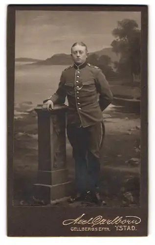 Fotografie Axel Carlborn, Ystad, Gellbergs Eftr., Portrait Soldat Mansson in Uniform vor einer Studiokulisse