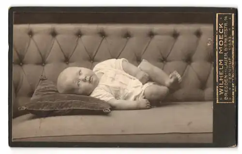 Fotografie Wilhelm Moeck, Dresden, Bienerstrasse 14, Kleinkind im Strampler auf dem Sofa