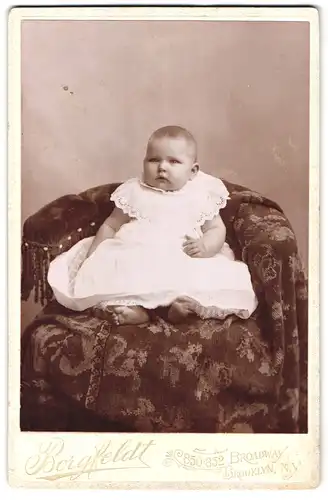 Fotografie Borgfeldt, Brooklyn / N.Y., Broadway 850-852, Portrait Kleinkind im weissen Kleid sitzt im Sessel