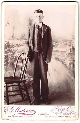 Fotografie C. G. Anderson, Kansas City / MO., Portrait junger Mann im karierten Anzug mit Schlips vor Studiokulisse