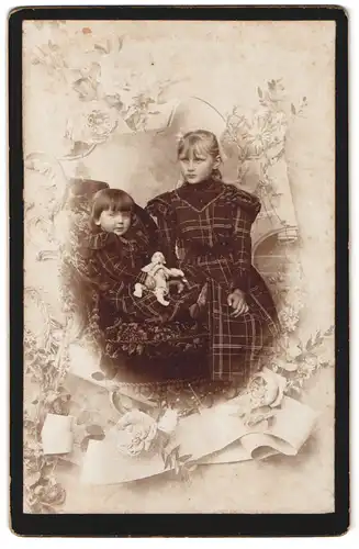 Fotografie Fotograf und Ort unbekannt, Portrait zwei Mädchen in karierten Kleidern mit Puppe in der Hand