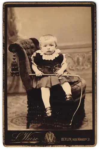 Fotografie L. Weise, Berlin, Neue Königstr. 51, Kleinkind in Kleidchen sitzt quer auf einem Sessel