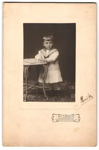 Fotografie Th. Lantin, Aachen, Friedrich Wilhelm Platz 10, Kleiner Junge in Matrosenoutfit lehnt an einem Tisch