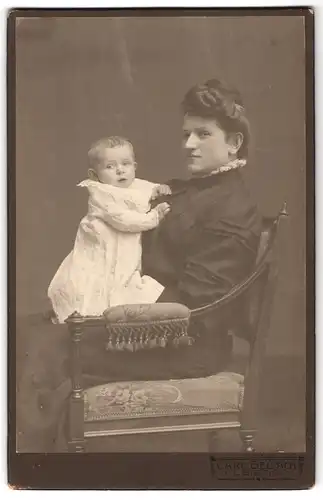 Fotografie Carl Bellach, Leipzig, Dame mit hochgesteckten Haaren sitzt auf Stuhl und hat ihr kleines Kind auf dem Schoss