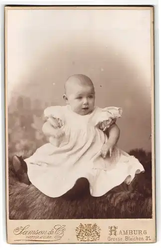 Fotografie Samson & Co., Hamburg, Grosse Bleichen 31, Baby im Taufkleid auf Felldecke sitzend