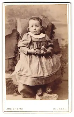 Fotografie Aug. Crome, Einbeck, Baustr., Portrait kleines Mädchen im Kleid mit Spielzeug Ente in der Hand