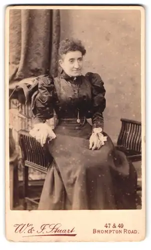 Fotografie W. & F. Stuart, London, 47 Brompton Road, gestandene Dame in Puffärmelkleid mit Taschenuhr