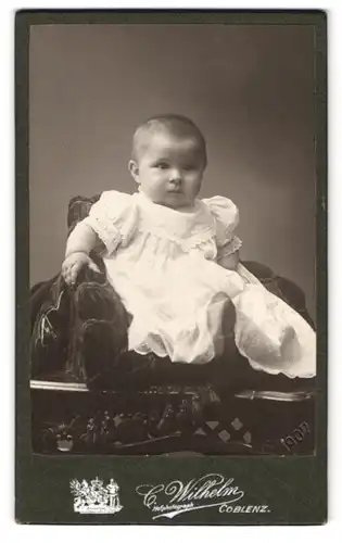 Fotografie C. Wilhelm, Coblenz, Löhrrondell 5a, Portrait Kleinkind im weissen Kleid sitzt im Sessel